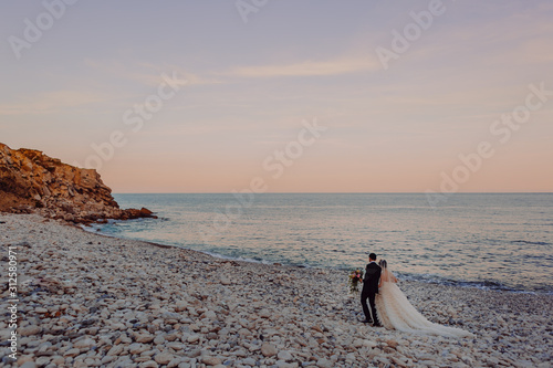Bride and Groom walking on the beach in England. Sunset colours background perfect wedding image of newlyweds.
