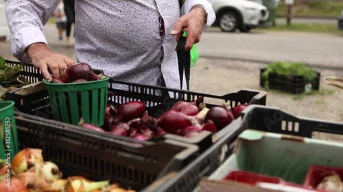 A short movie shot in close up detail as an elderly shopper buys fresh and organic red onions from a market stand. during a biological farmers market