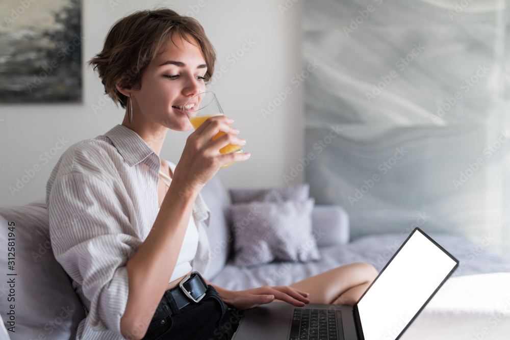 Young woman drinking orange juice and surfing in the internet at home