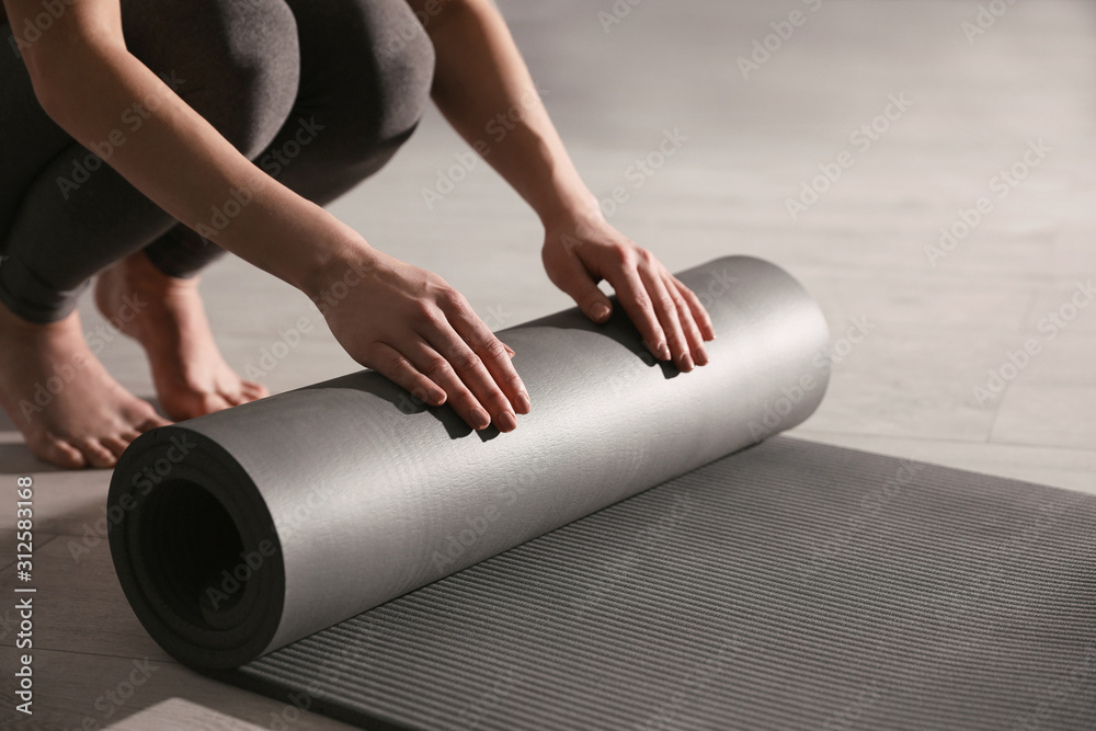 Woman rolling yoga mat in studio, closeup - obrazy, fototapety, plakaty 