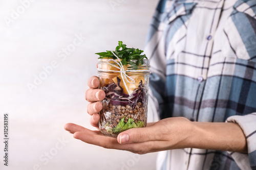 Woman holding glass jar with healthy meal, closeup photo