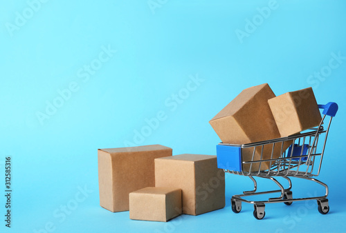 Shopping cart and boxes on light blue background, space for text. Logistics and wholesale concept