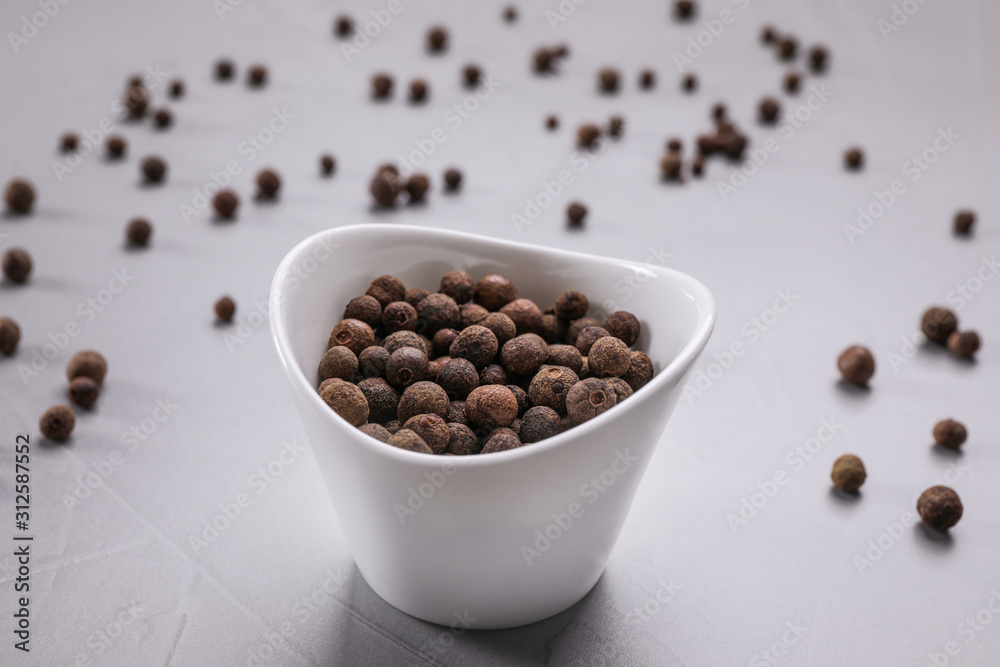 Black peppercorns in bowl on grey table Black peppercorns in bowl on grey table