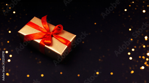 Golden gift with a red ribbon on a black background. Rozhdenvensky and New Year s concept. discounts and black friday