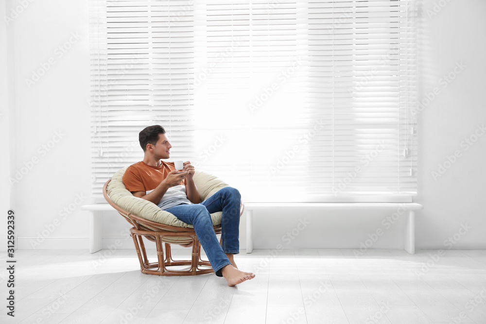 Attractive man relaxing in papasan chair near window at home. Space for text Attractive man relaxing in papasan chair near window at home. Space for text