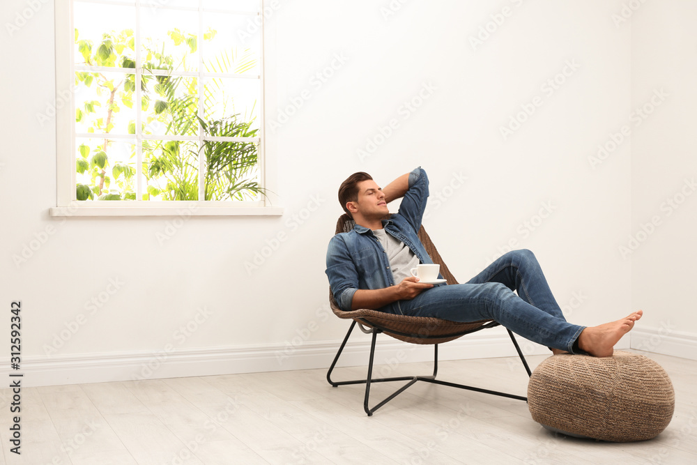 Attractive man relaxing in armchair near window at home. Space for text