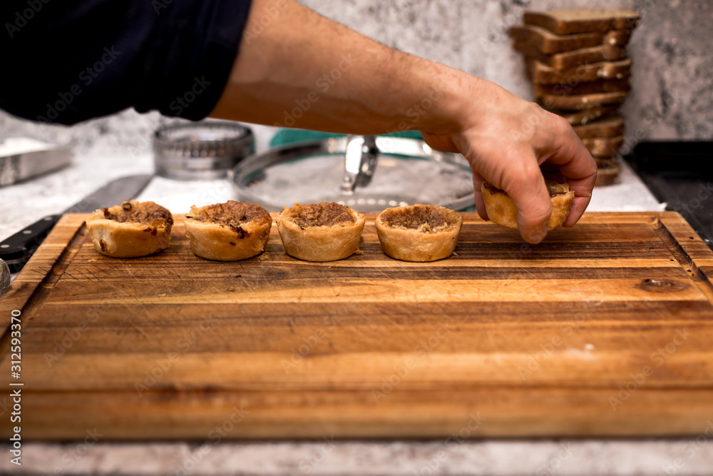 A row of butter tart cookies being laid on a wooden board by a pastry chef.