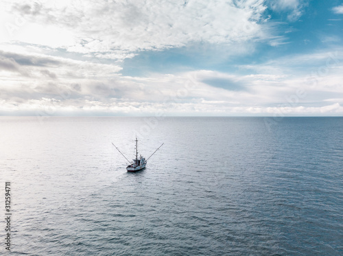 A small old fishing trawler on the open ocean with clouds on the horizon.