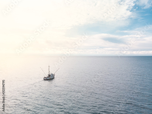A small old fishing trawler on the open ocean with clouds on the horizon. © Adam