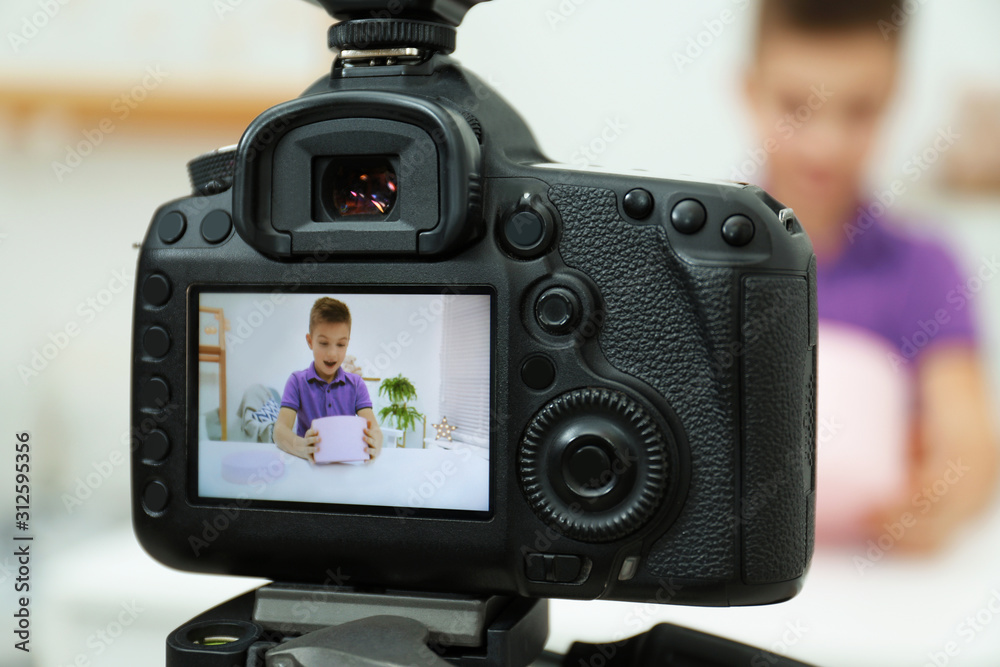 Emotional little blogger with box recording video at home, focus on camera