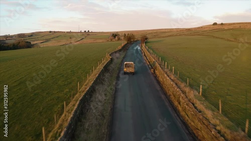 Aerial footage following a vehicle with a dog in the back as it travels across rural farm land in the English Countryside during a beautiful sunset