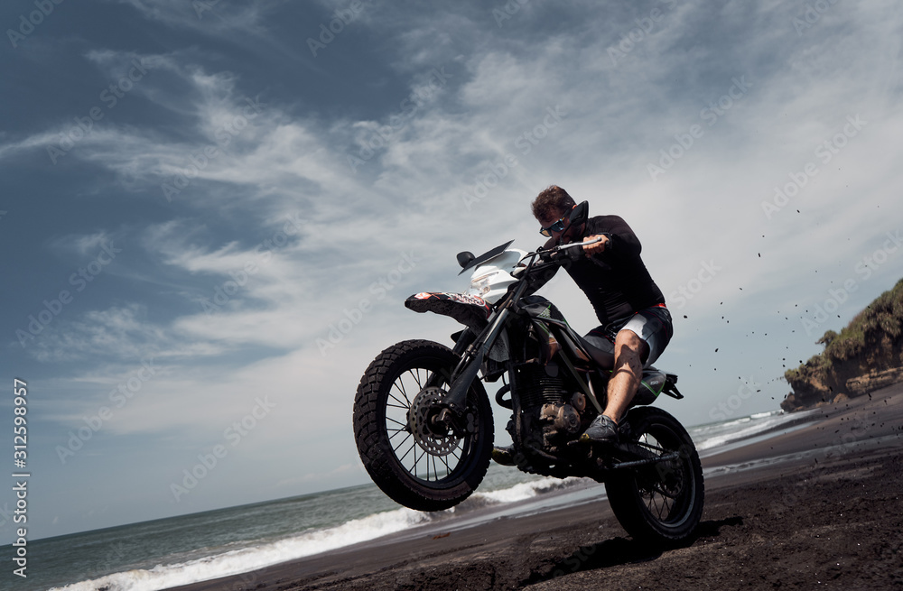 Fototapeta premium Mężczyzna jedzie na motocyklu na plaży z czarnym piaskiem oceanu
