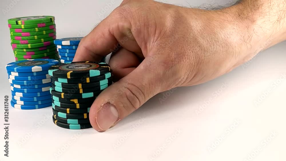 Male hand moving a black stack of poker chips across the white table, ISOLATED, SLOMO, STILL Male hand moving a black stack of poker chips across the white table, ISOLATED, SLOMO, STILL