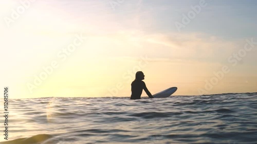 Longboarder woman waits on her board for the best wave, bathed in yellow golden light photo