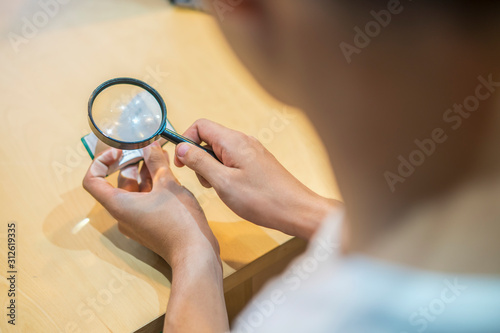 Man use magnifying glass for searching data in a little book at university library