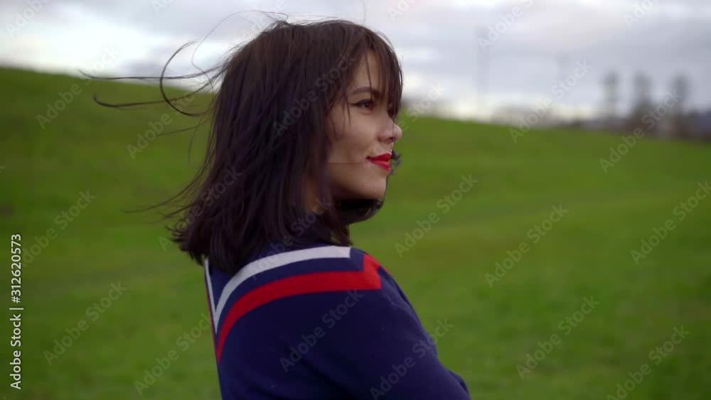 portrait of a dark-haired young pretty girl walking on the street on the grass, she has bright makeup and red lipstick, her hair fluttering in the wind. She has a piercing in her nose, above her lip. portrait of a dark-haired young pretty girl walking on the street on the grass, she has bright makeup and red lipstick, her hair fluttering in the wind. She has a piercing in her nose, above her lip.