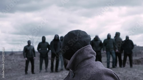 Man sits in a chair and looks at a group of masked criminals. Footage. A meeting place for gangsters. OPG grouping photo