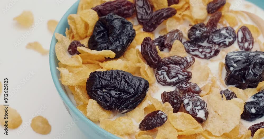 Truck shot of Cornflakes prunes and resin with milk and wooden spoon in the blue bowl on white background Truck shot of Cornflakes prunes and resin with milk and wooden spoon in the blue bowl on white background