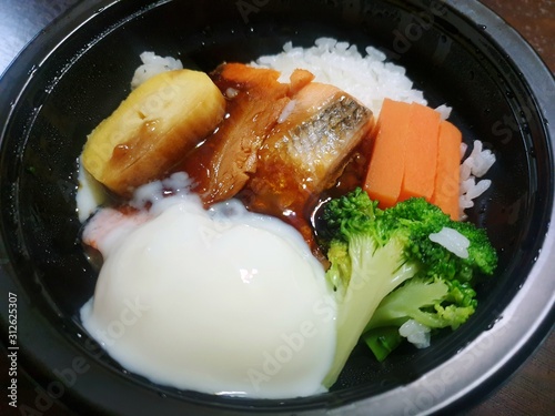 Japanese food style, Top view of rice topped with grilled salmon teriyaki sauce, soft boiled egg and vegetable in black bowl as a background, Ready to eat or serve