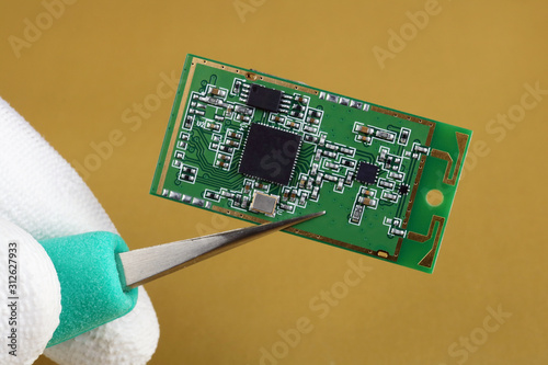 IT industry engineer holds with tweezers mini wireless bluetooth  module for mobile devices macro photo