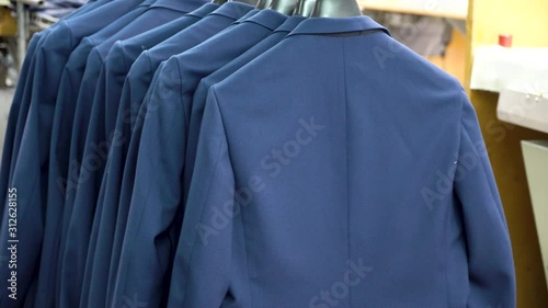 A row of new men's suits on hangers at a textile factory. Blue suits, jacket hanging on a hanger ready for further processing and sale. 4k footage.