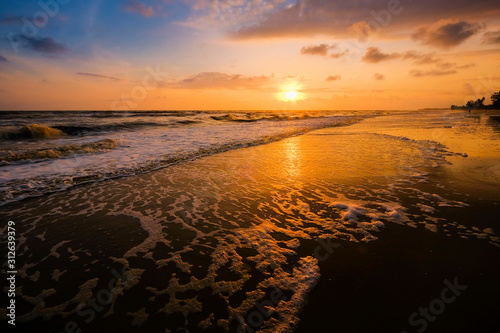 Beautiful cloudscape over the sea with soft wave of blue ocean on sandy beach during sunrise.