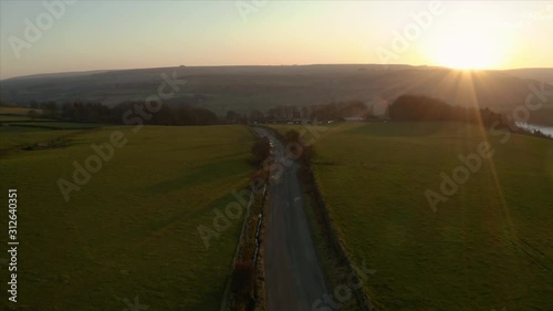 Aerial footage along a small narrow country road through hills and farm land in the Peak District National Park, UK, during a beautiful sunset, Winter 2019 photo