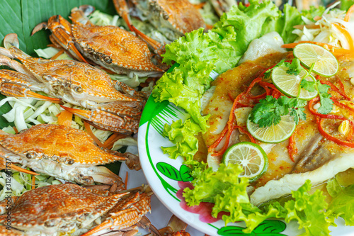 Steamed fish with lemon in a saucer with green vegetables and steamed crabs.