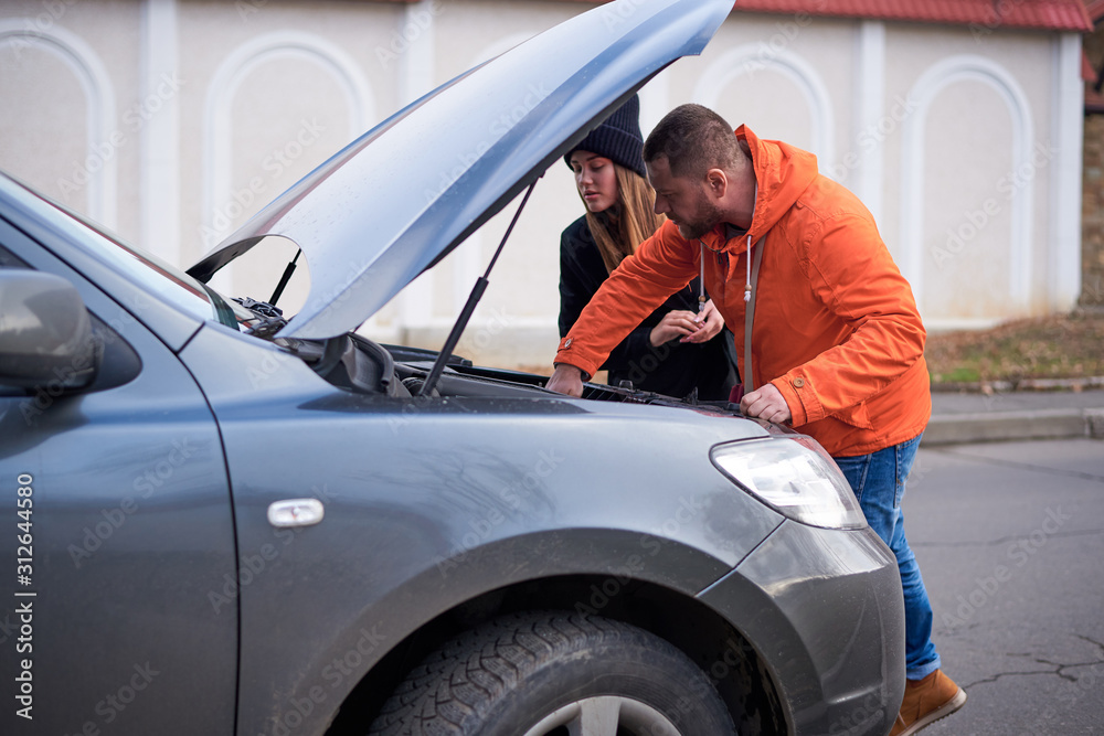Young couple near a car with an open hood on the road.