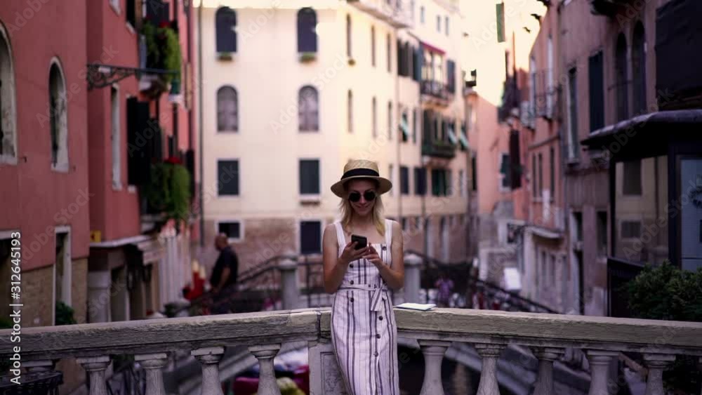 Slow motion effect of happy caucasian female tourist dialing number to friend and discussing italian trip while resting on Venice bridge and feeling good Slow motion effect of happy caucasian female tourist dialing number to friend and discussing italian trip while resting on Venice bridge and feeling good