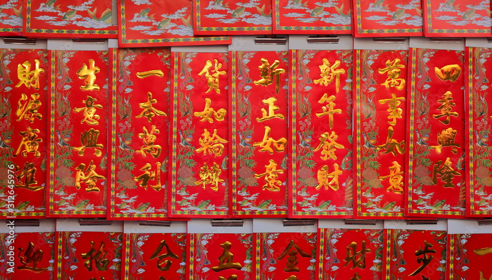 Closeup chinese new year greetings printed with gold color on red paper hanging in front of a store, the chinese words mean happy new year, wealth, prosperity and wishes come true Closeup chinese new year greetings printed with gold color on red paper hanging in front of a store, the chinese words mean happy new year, wealth, prosperity and wishes come true