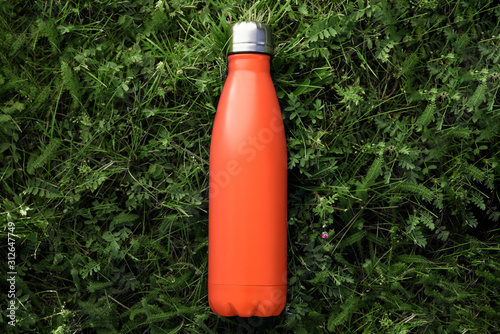 Top view of reusable steel thermo water bottle with mockup on green grass, lush lava color.