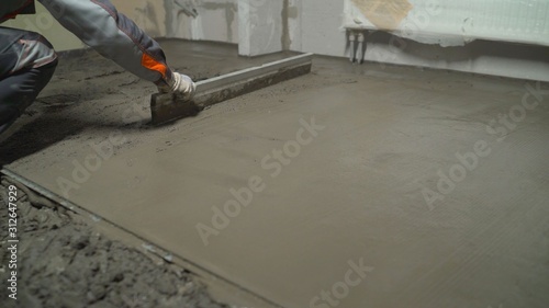 Leveling concrete with trowels, laborer spreading poured concrete. Indication of mortar on the floor and leveling of concrete floors