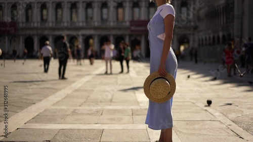 Slow motion, caucasian beautiful carefree female tourist dressed in stylish blue sundress standing on historic San Marco Square and enjoying summer warm weather during Italian weekend in Venice city