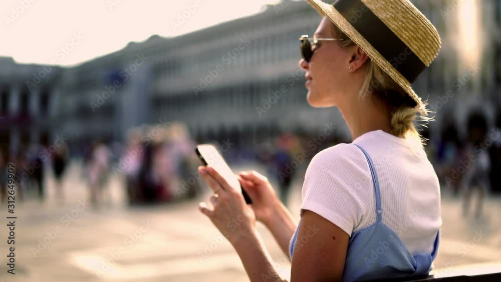 Cheerful female tourist holding mobile phone and typing text message during chatting with friends via smartphone application and making pictures of San Marco Square. Female using mobile phone app