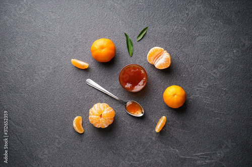 Tangerine jam with tangerines and green leaves on a dark background flat lay.