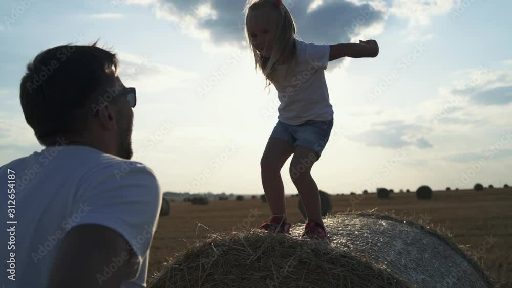 Portrait of father catches his lovely daughter, throws up in hands at haycock