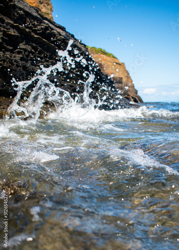 a sea wave is breaking on stones on a bright summer day. Close-up. Spray fly right into the frame. © Anastasiya