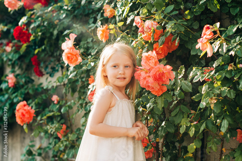 Outdoor summer portrait of adorable 5 year old little girl playing in summer garden with roses