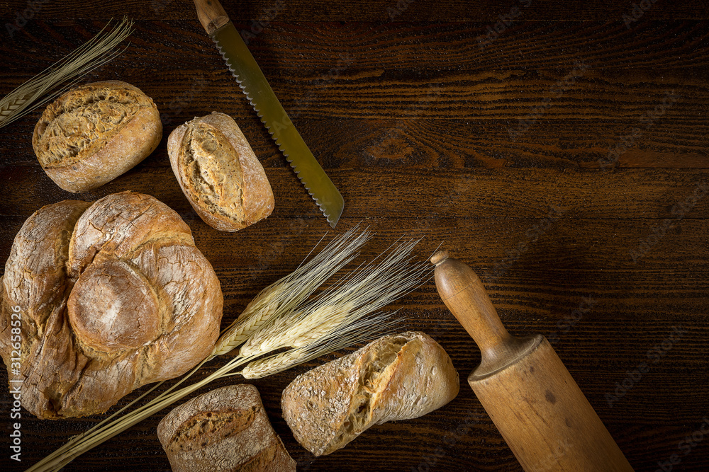 Traditional fresh bread with a blade of wheat on a wooden background.