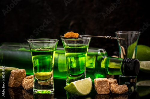 absinthe shots with sugar cubes. absinthe poured into a glass. bottle of absinthe with brown sugar and lime isolated on black background photo