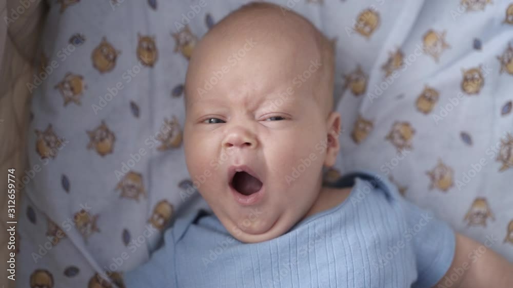 Newborn baby lying in a cradle and yawning at camera. Top view