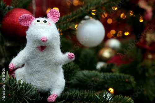 White knitted toy rat on background of fir branches and golden lights, New Year card. Chinese Year of Rat, Zodiac symbol 2020