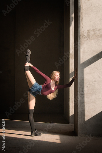 Blonde dancer stands on fingers on a gray background. Dance pose, dance, body shape, fitness, training, strength, sunlight