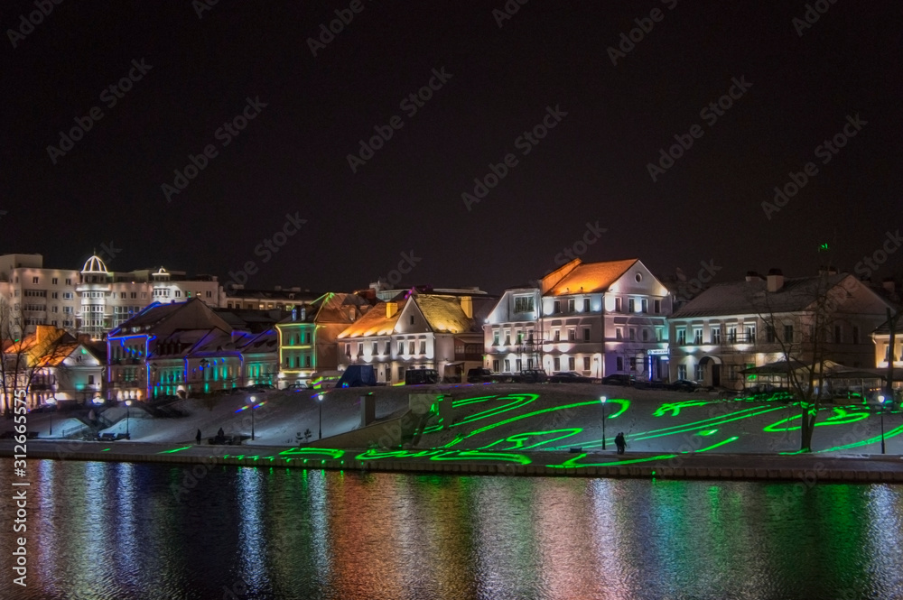 Christmas night neon glowing cityscape. Bright city lights reflected in the water. Minsk Belarus. December 31 2019