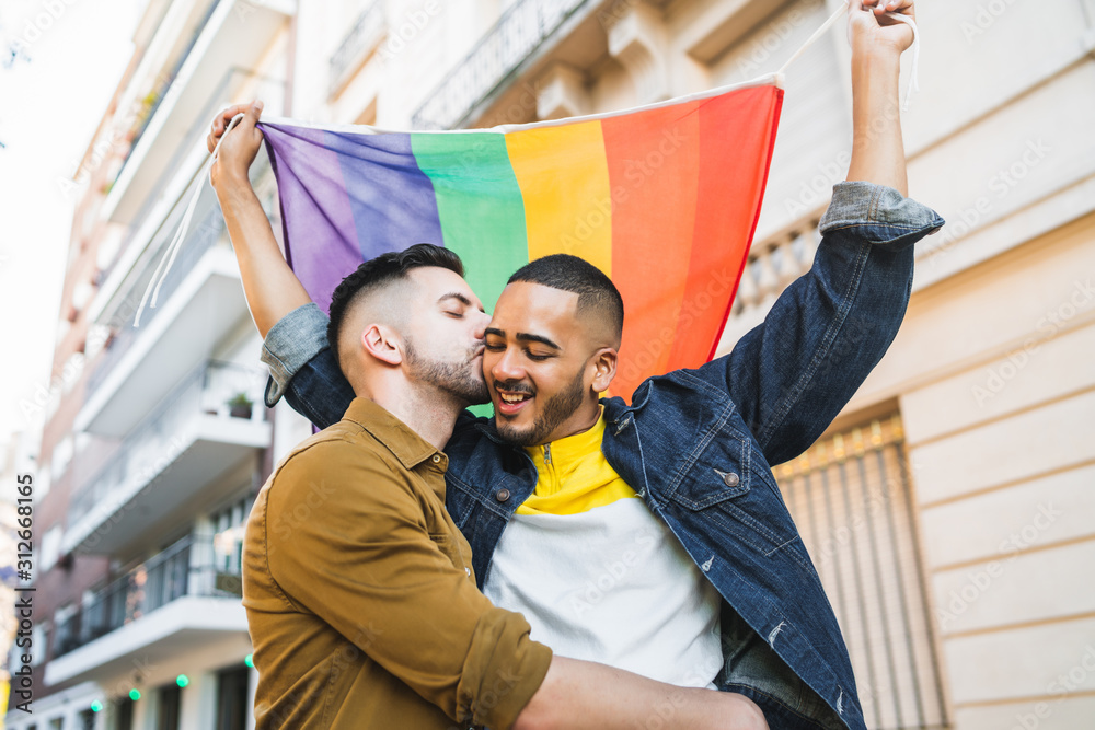 Gay couple embracing and showing their love with rainbow flag. foto de ...