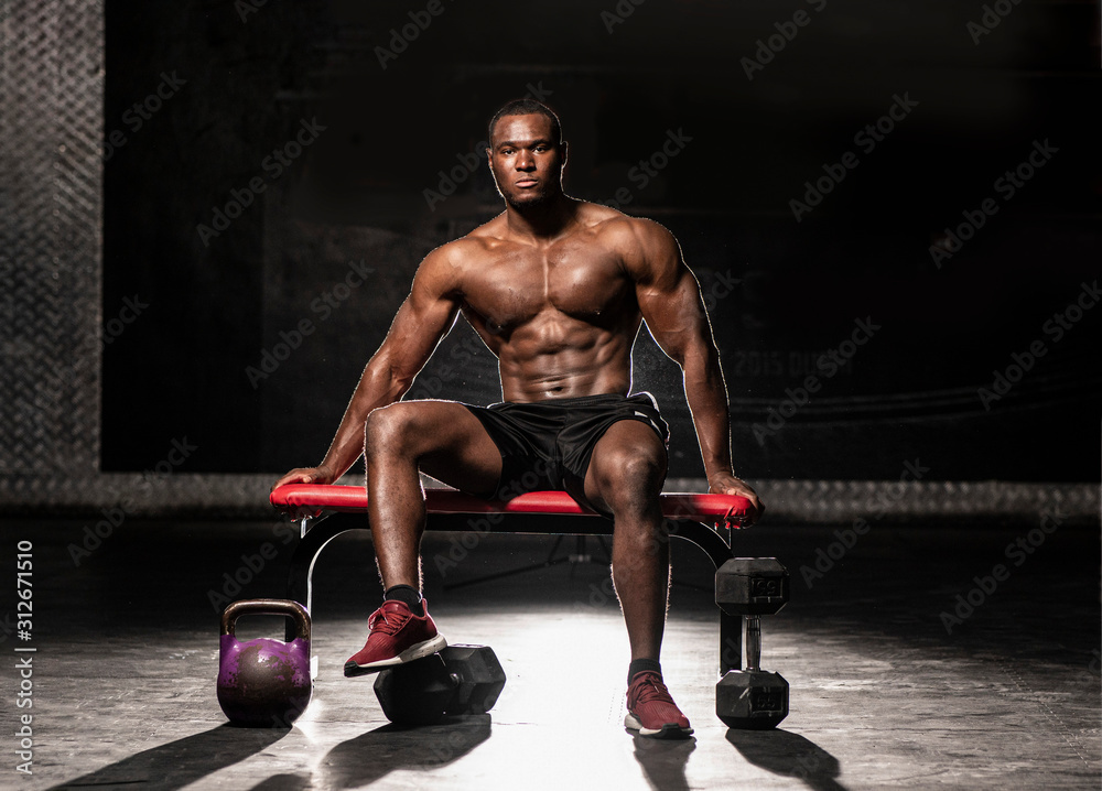 Muscular African American shirtless, sweaty male bodybuilding athlete  sitting on a bench showing his six pack abs in a dark grungy gym with  dramatic lighting flare Stock Photo | Adobe Stock
