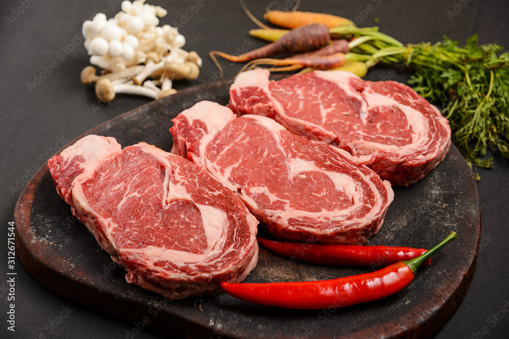 Three pieces of fresh beef meat with vegetables on wood, uncooked	