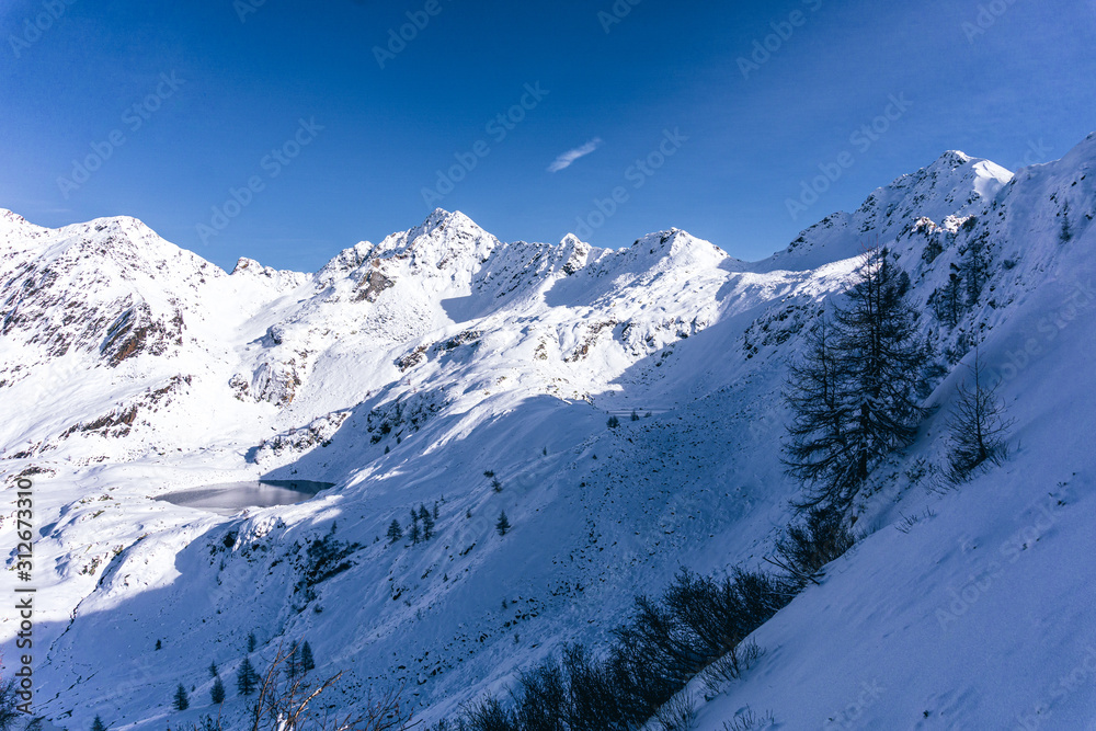 The snowy mountains, the nature and the landscape of the Valtellina after the first snowfall of the season in the Alps, near the town of Tartano, Italy - November 2019.