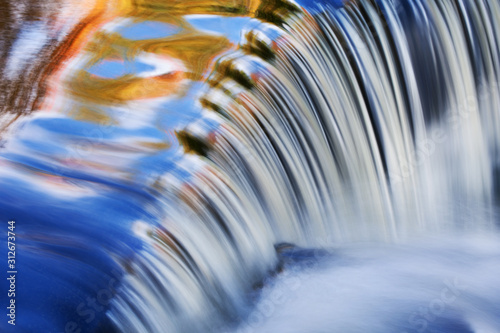 Bond Falls cascade captured with motion blur and illuminated by reflected color from sunlit autumn maples and blue sky overhead, Michigan's Upper Peninsula, USA